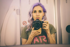 violet hair girl taking a selfie in the mirror of the bathroom on an airplane violet hair girl taking a selfie in the mirror of the bathroom on an airplane